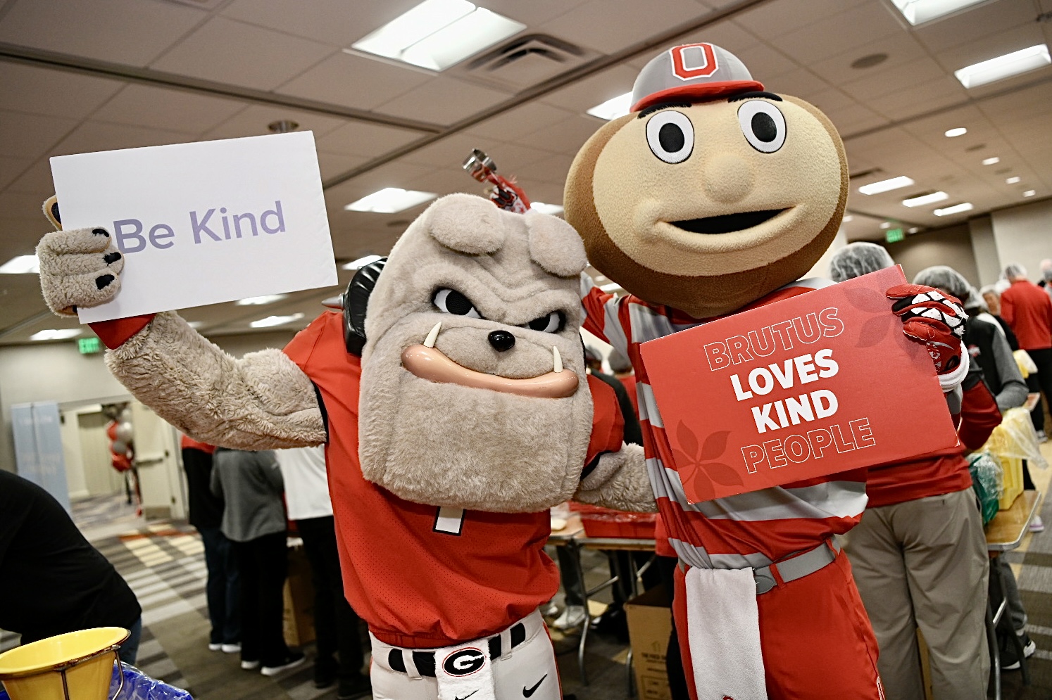 Brutus Buckeye and the University of Georgia Bulldog holding kindness signs at the food packing event in Atlanta.