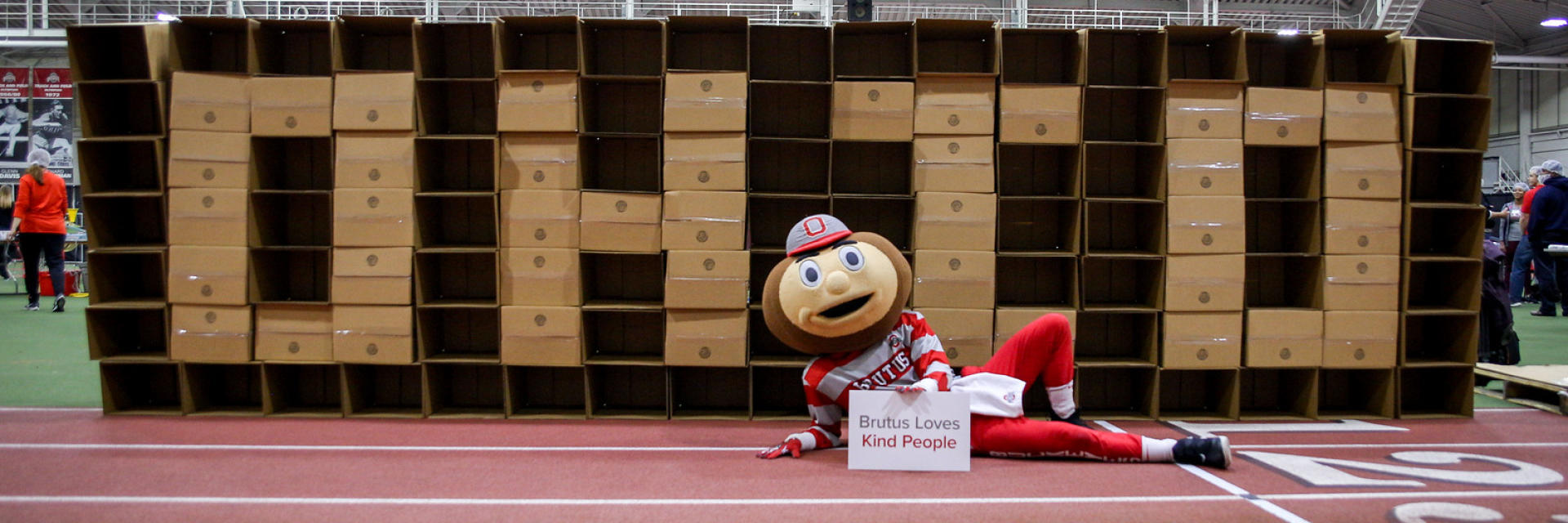 Brutus Buckeye holding a sign that states 'Brutus Loves Kind People'