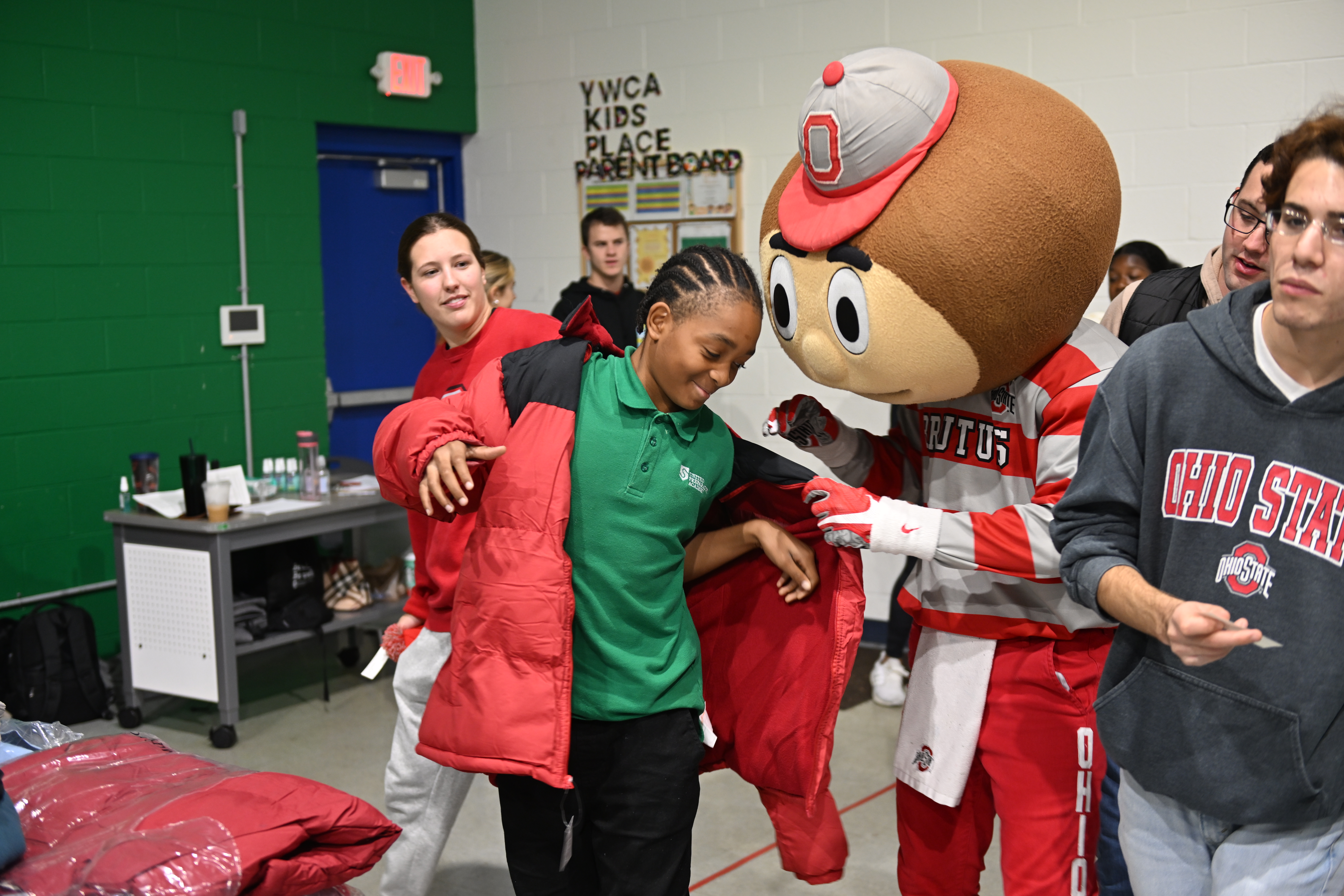 A young boy having Brutus Buckeye help him get a coat on.